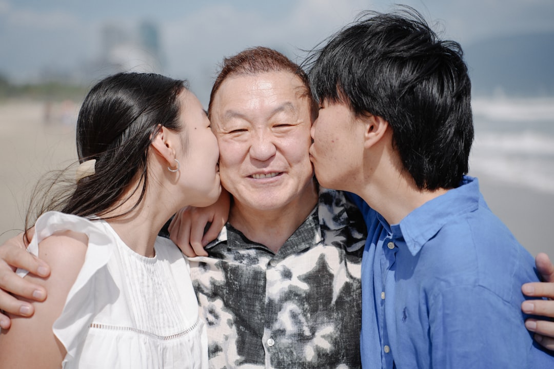 Two children kiss their smiling grandfather on the beach.